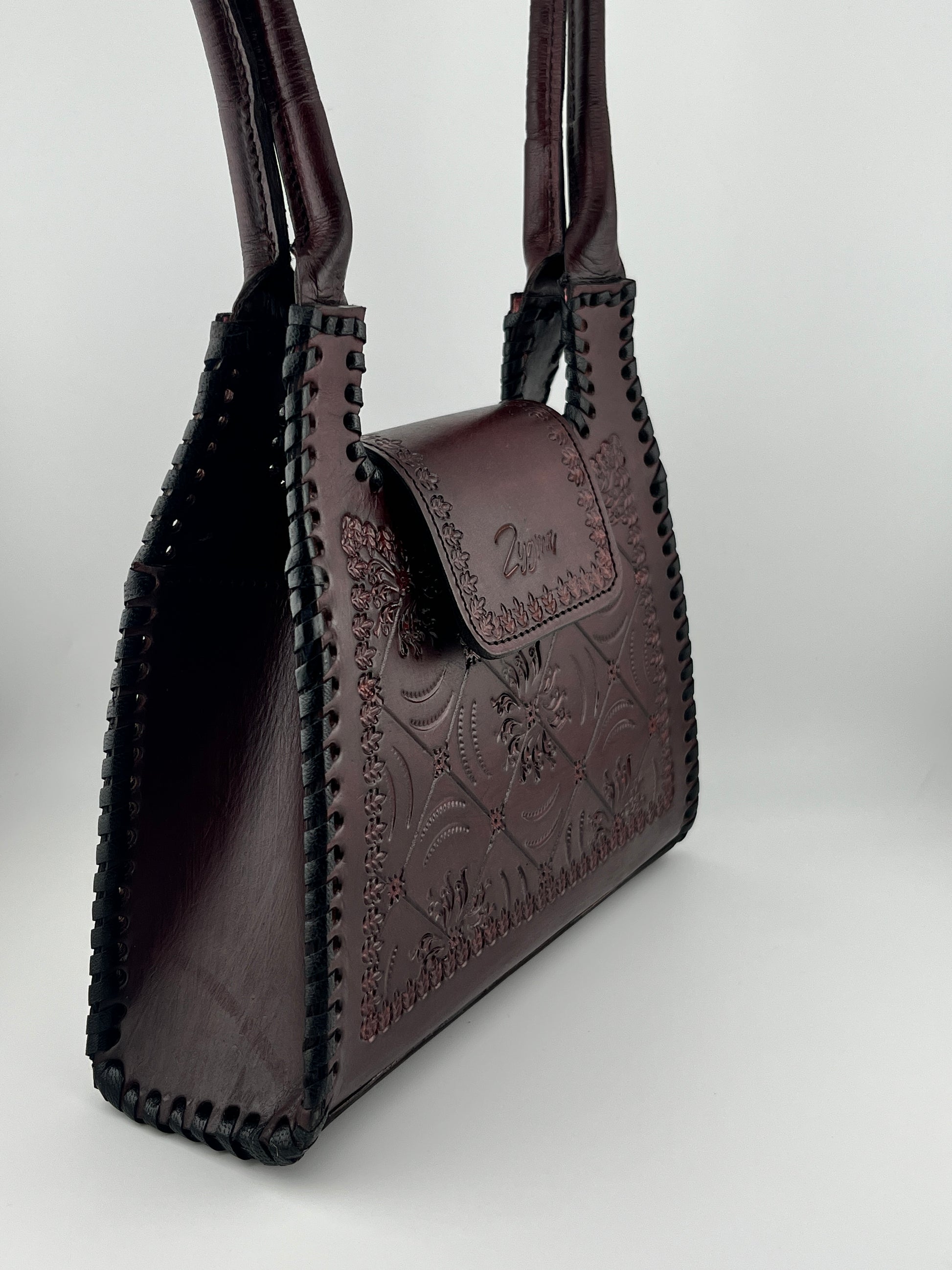 Close-up of a brown leather handbag with intricate designs on a white background