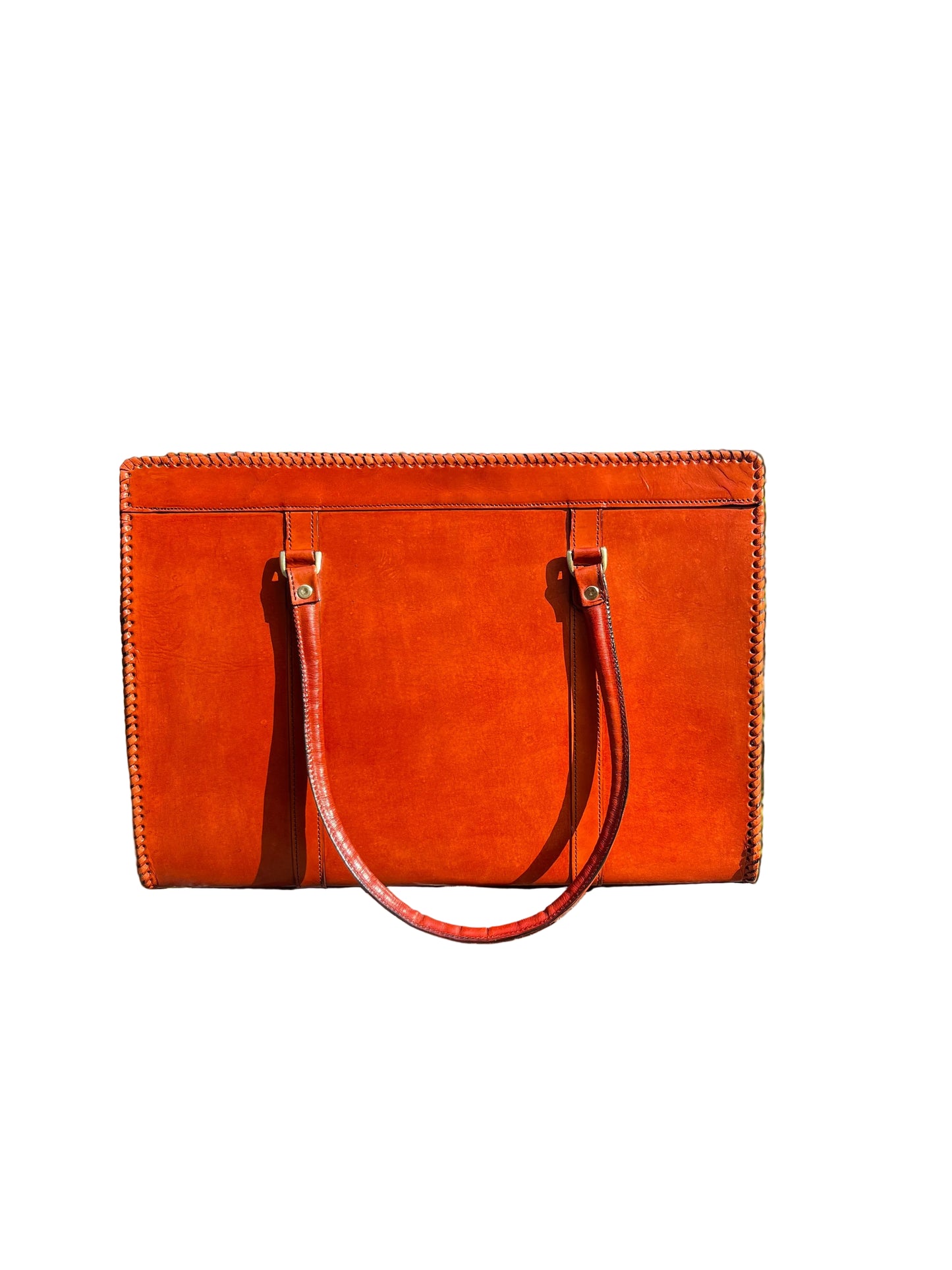 Brown leather handbag on a stone ledge with greenery in the background