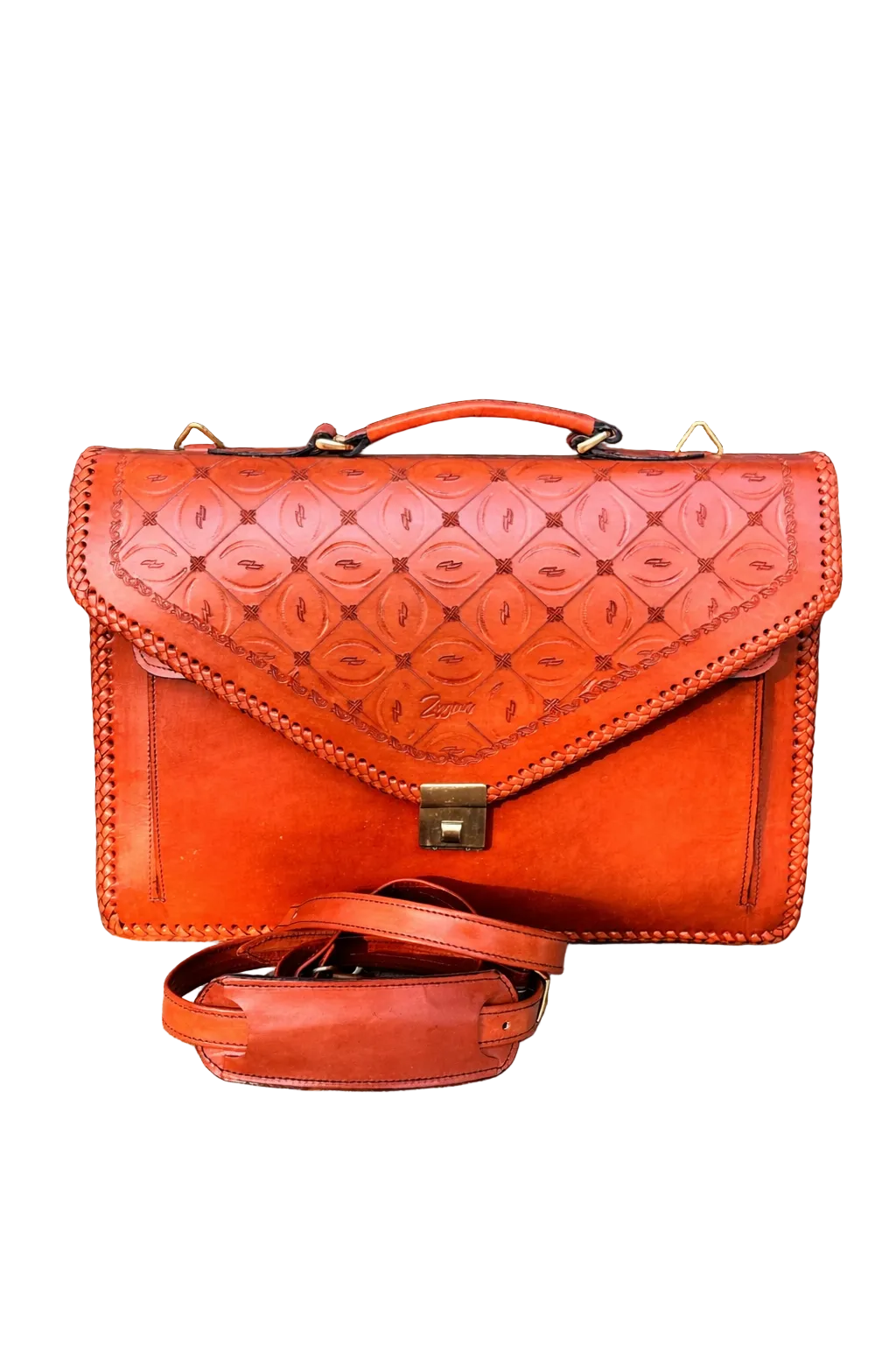 Orange leather handbag with embossed pattern on a stone surface with greenery in the background